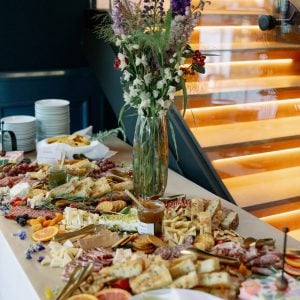 Elegant charcuterie display with assorted cheeses, cured meats, fruits, and flowers, set in a modern venue, ideal for wedding rehearsal dinners and welcome events at Belvedere Lenox.
