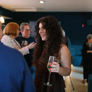Woman with curly hair holding a champagne glass, smiling and engaging in conversation at a stylish event venue, reflecting the elegant atmosphere of Belvedere Lenox for special celebrations.