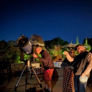 Group of people enjoying stargazing with a telescope at night, highlighting a social gathering atmosphere perfect for memorable events at Belvedere Lenox.
